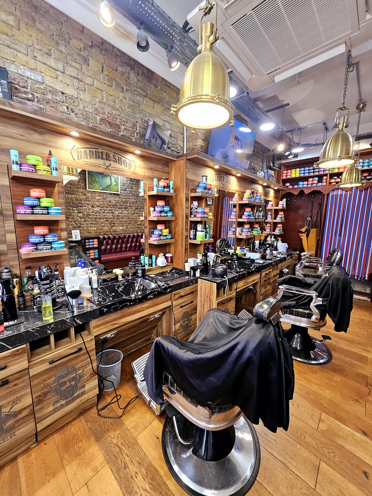 The barbershop interior looking down the row of chairs, exposed brick, mirrors, brass pendant lamps and a wooden floor.